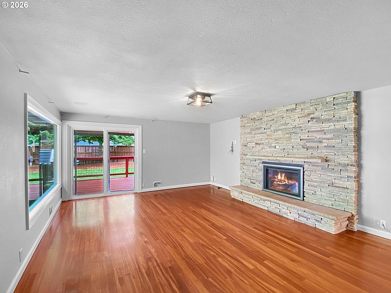 The refreshed living room with refaced stone fireplace, hardwood floors, fresh paint, and sliding glass doors looking out to the backyard deck